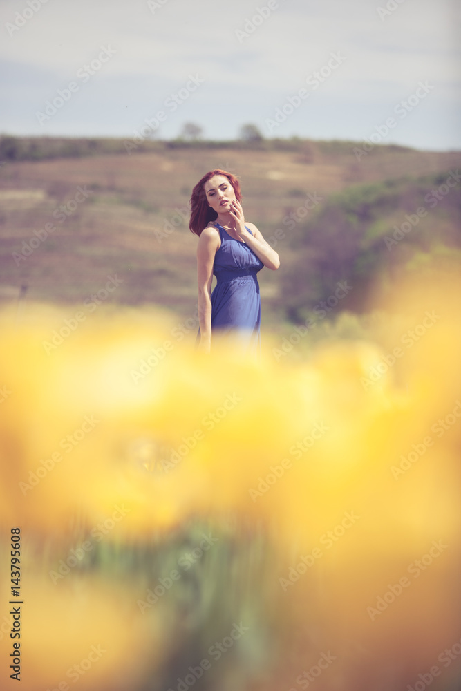Gorgeous woman in blue dress in flower field in sunny day. Outdoor shooting. Lifestyle and relaxation