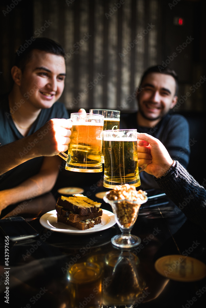 Friends drinking beer and clinking glasses at bar or pub