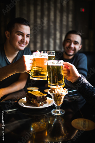 Friends drinking beer and clinking glasses at bar or pub