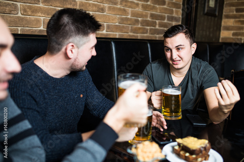 Handsome young man toasting with beer and discussing while sitting with his friends in beer pub