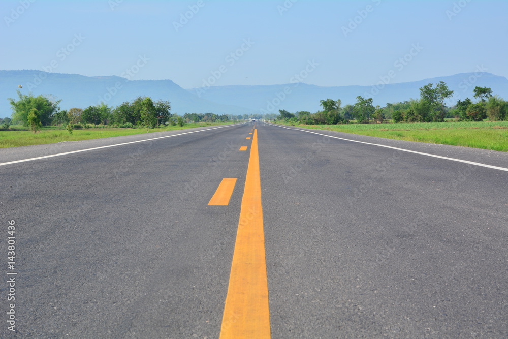 asphalt road through the green field and clouds on blue sky in summer day
