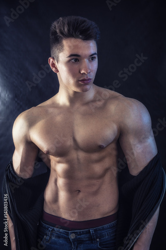 Handsome young muscular man shirtless wearing jeans, isolated on black background in studio shot