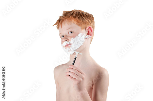 boy redhead with freckles naked to the waist, playing with the razor and foam isolated on white.