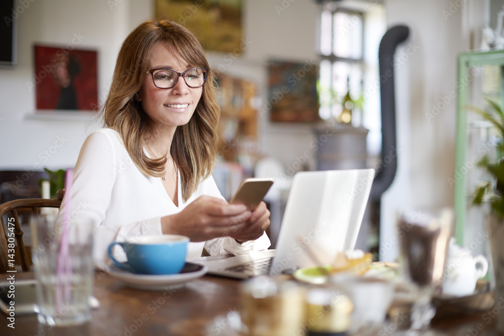 Woman working on laptop. Shot of a smiling confident businesswoman using mobile phone and computer while working in cafe. Woman working on laptop. Shot of a smiling confident businesswoman using mobile phone and computer while working in cafe.