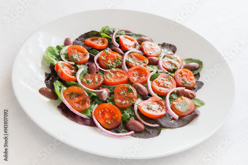 carpaccio of cherry tomatoes on salad leafs decorated with kalamata olives and red onion and dressed with olive oil and lemon juice