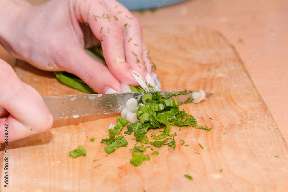 The girl cuts onions on a wooden board