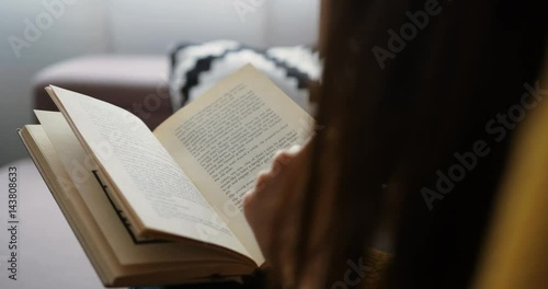 Close up woman reading interesting book while sitting on the couch at home. Close up back view. Close up book