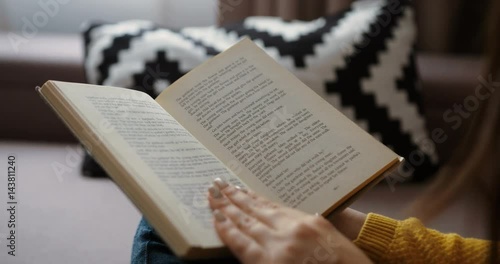 Close up woman hands reading interesting book while sitting on the couch at home. Close up back view. Close up book