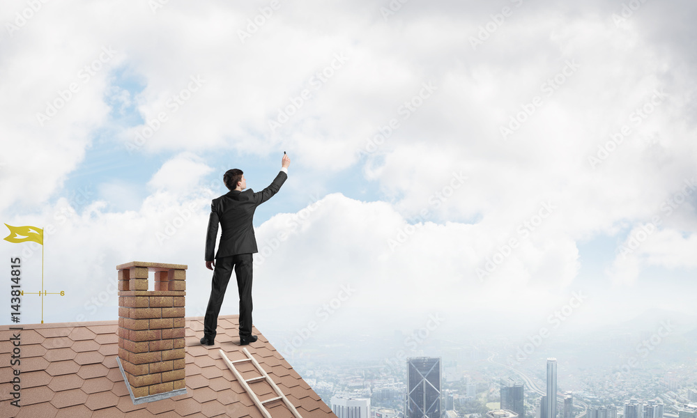 Businessman on house roof touch empty space. Mixed media Businessman on house roof touch empty space. Mixed media