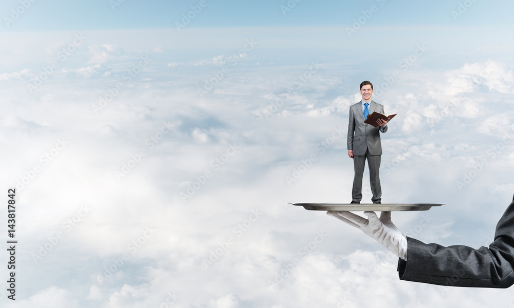 Businessman on metal tray with red book in hands against blue sky background