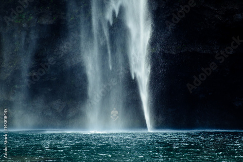 Man meditates sitting under a waterfall in lotus flower position