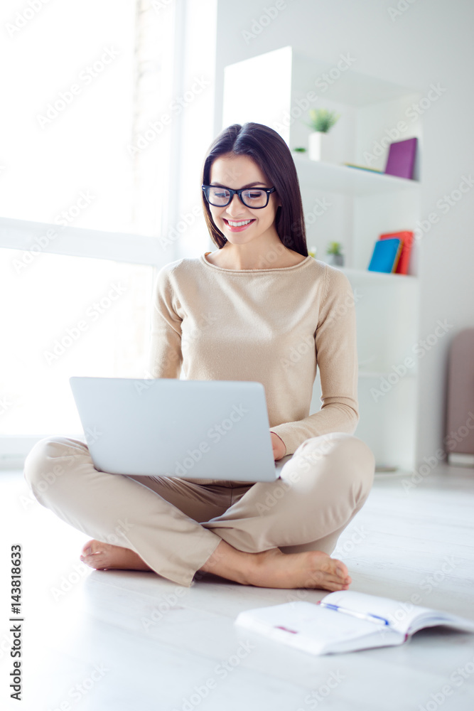 Obraz premium Vertical portrait of young pretty woman in glasses sitting on the floor at home and using laptop