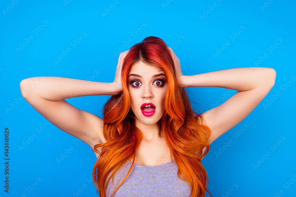 Obraz premium Close-up of attractive cute girl with long ginger ombre fair hair with shocked face touching head with hands while standing on blue background