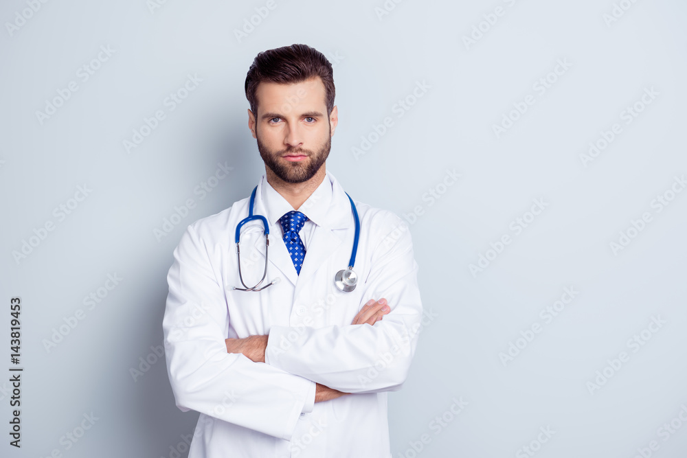 Portrait of serious handsome male doctor with crossed hands on gray background Portrait of serious handsome male doctor with crossed hands on gray background