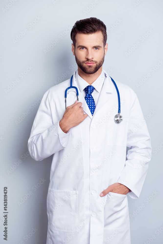 Portrait of serious handsome young male doctor holding hand in pocket standing on gray background Portrait of serious handsome young male doctor holding hand in pocket standing on gray background