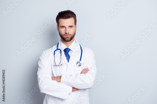 Portrait of serious handsome male doctor with crossed hands on gray background