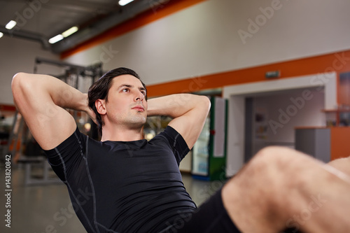 Athletic man in the black sportwear working with his abdominal on simulator in gym.