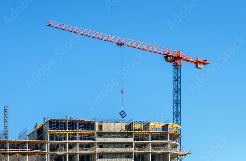 Construction site. Construction cranes and high-rise building under construction against blue sky.