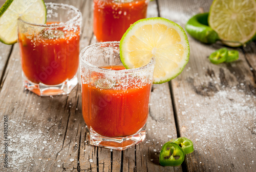 Mexican traditional alcohol drink. Sangrita, with tequila, tomato juice, hot spices, chili and lime.Analogous bloody mary. On rustic wooden table, copy space photo