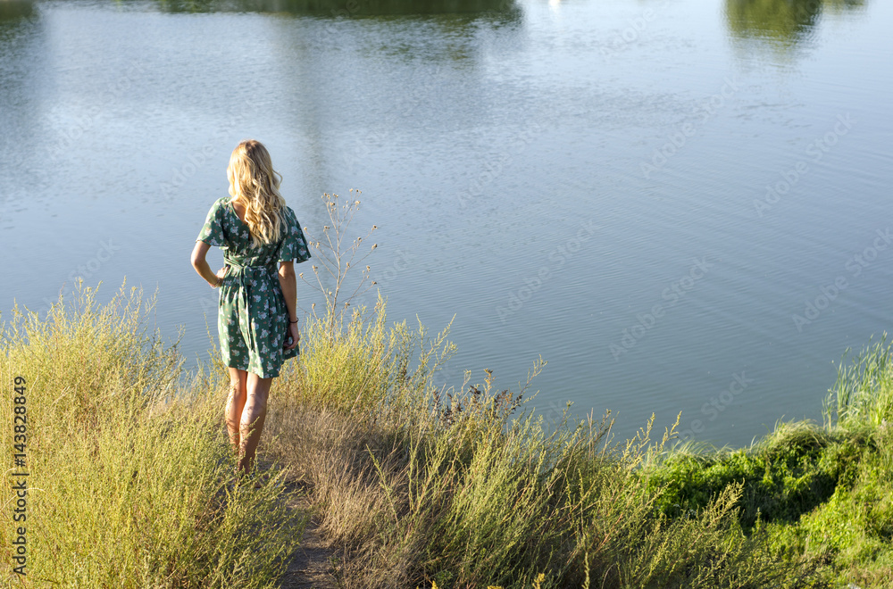 Young woman stands on the river bank and looks at the water Young woman stands on the river bank and looks at the water