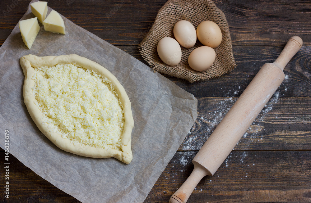 Khachapuri with eggs on sackcloth, flour, eggs and rolling pin on black table Khachapuri with eggs on sackcloth, flour, eggs and rolling pin on black table
