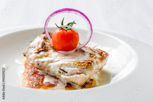 Tasty roasted pork pieces with cheese sauce, tomato and onion on white plate close up. Selective focus image