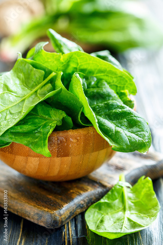 Wooden bowl with fresh spinach leaves in water drops.