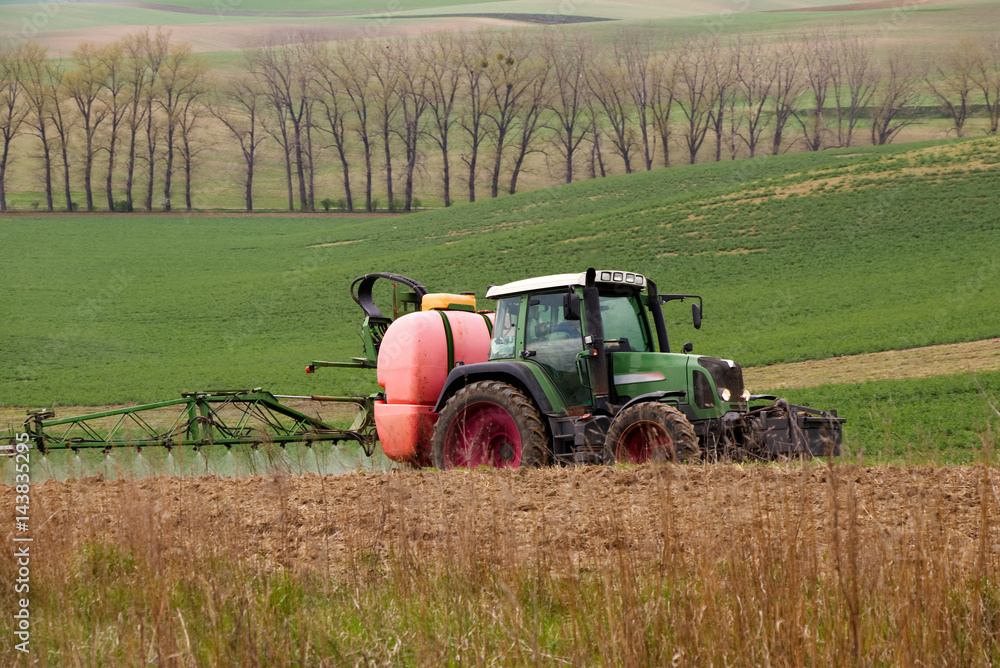 Obraz premium Farm machinery spraying insecticide to the green field, agricultural natural seasonal spring background. Tractor sprinkling pesticides against bugs on agricultural field