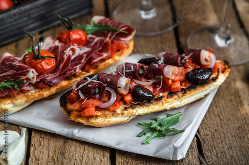 Wine appetizer set. Glass of red wine, brushettas with fresh tomato and jamon on over rustic grunge wooden background