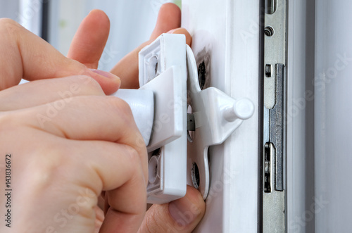 Close-up hands of locksmith  installing window limiter on plastic frame.