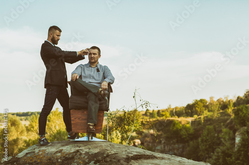 Bearded barber giving a haircut to his male client outdoors