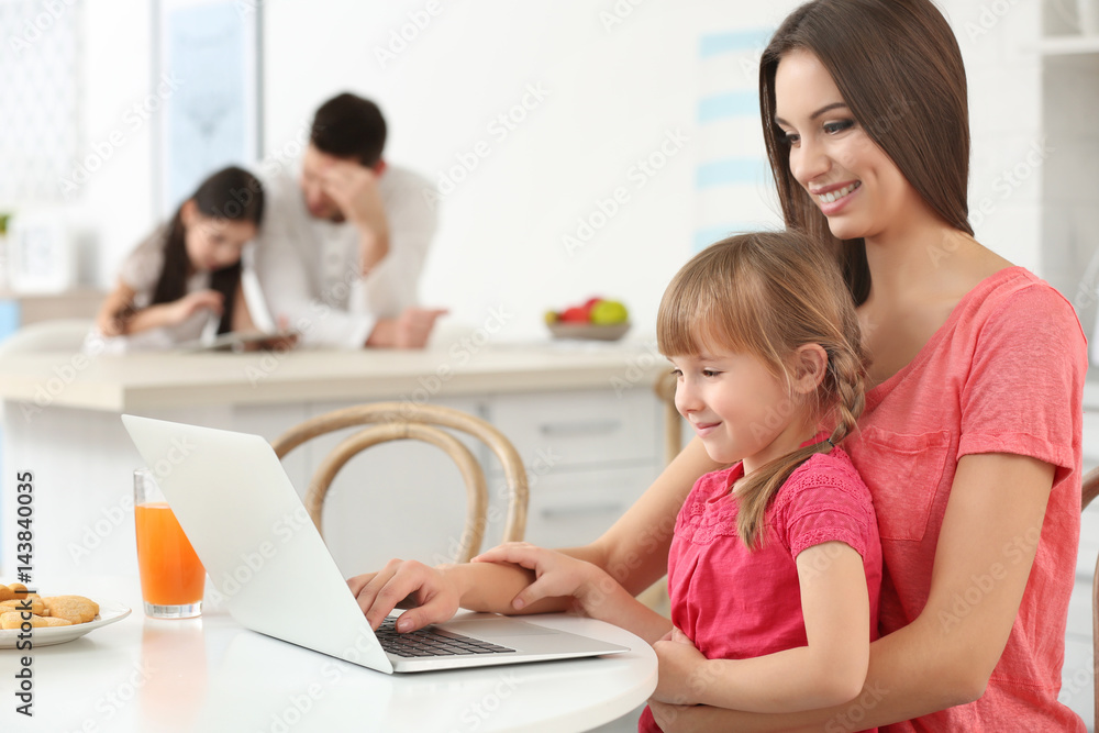 Young woman and girl with laptop sitting at kitchen table Young woman and girl with laptop sitting at kitchen table