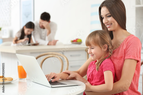 Young woman and girl with laptop sitting at kitchen table