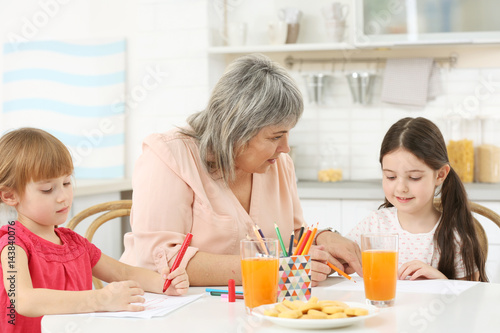 Little girls with grandmother drawing at kitchen table