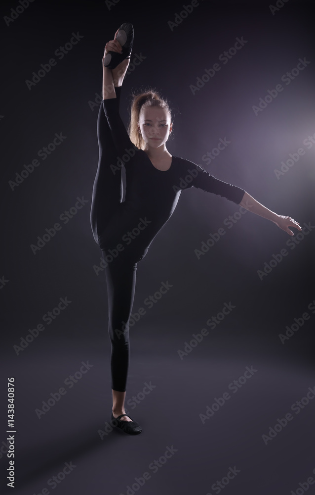 Obraz premium Young girl doing gymnastics on dark background