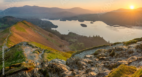 Sun rising above horizon at Derwentwater illuminating the landscape with vibrant Spring light.