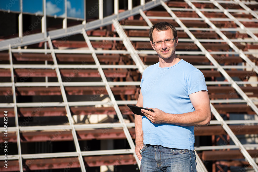 Young man with tablet stands on the background of building structures Young man with tablet stands on the background of building structures