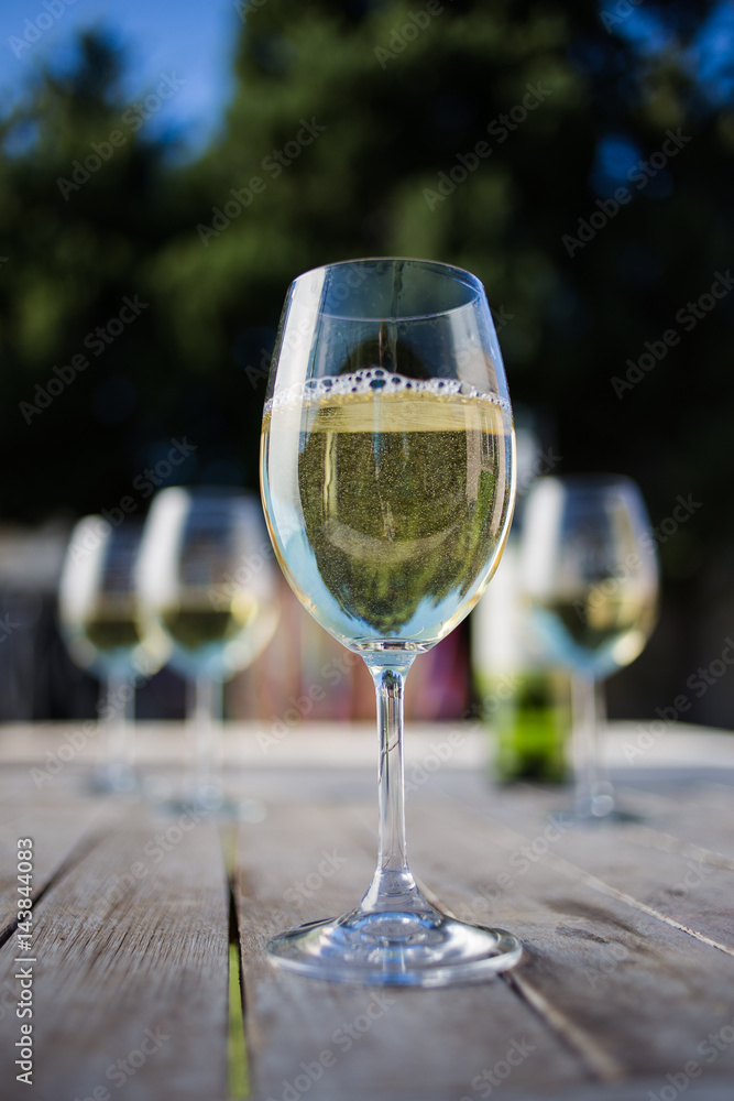 Close up image of white wine being poured into a glass on a wooden table outside with natural light Close up image of white wine being poured into a glass on a wooden table outside with natural light