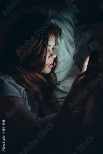 woman lies in bed and looks into phone