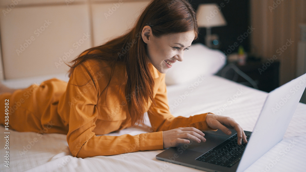 woman lies on the bed and looks at the laptop, typing on the keyboard woman lies on the bed and looks at the laptop, typing on the keyboard