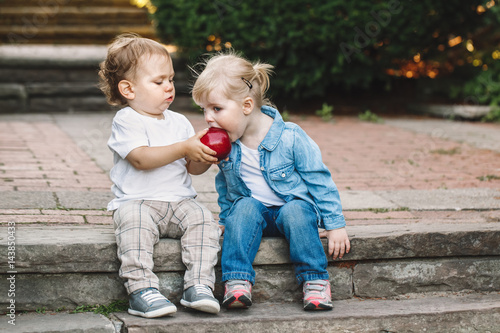 Group portrait of two white Caucasian cute adorable funny children toddlers sitting together sharing eating apple food, love friendship childhood concept, best friends forever