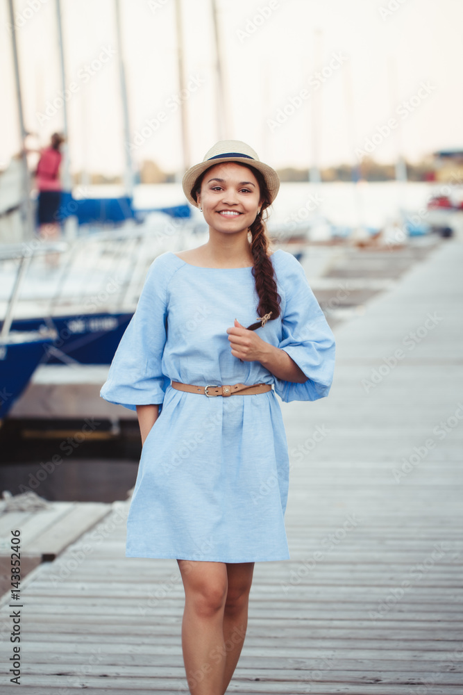 Portrait of white Caucasian brunette woman with tanned skin in blue dress by seashore lakeshore with yachts boats on background on water, lifestyle summer hobby leisure concept