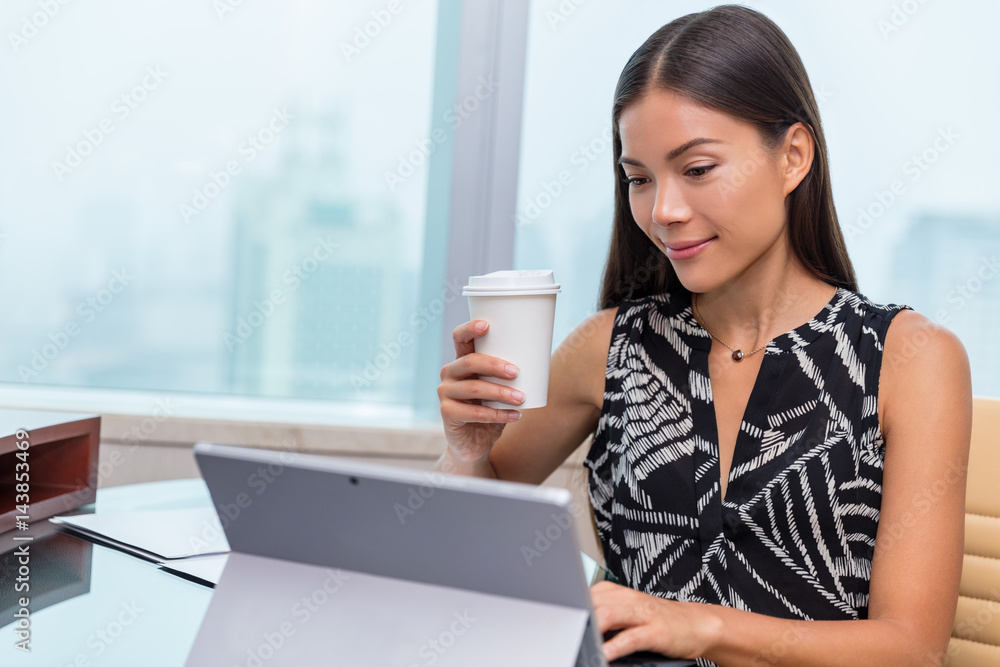 Portrait of a serious businesswoman using laptop at office desk while drinking a coffee cup. Asian woman working on computer at home.