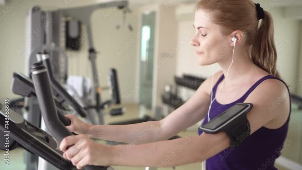 Beautiful fit young woman in a gym doing exercises on a velosimulator. Listening music doing sport. Beautiful fit young woman in a gym doing exercises on a velosimulator. Listening music doing sport.