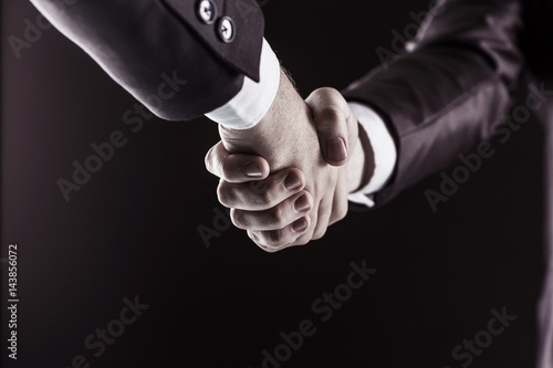 concept of a reliable partnership: a close-up of handshake of business partners on a black background.