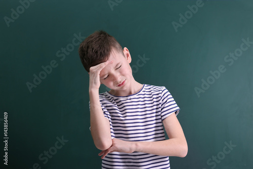 Cute boy suffering from headache on color background