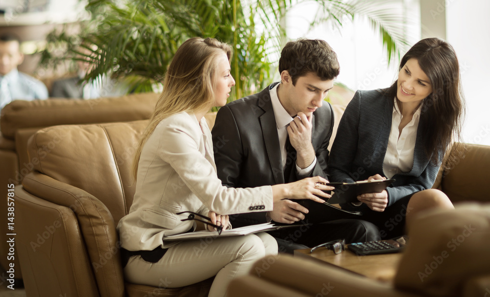 Business team discussing working papers sitting on the couch in the lobby of a modern office Business team discussing working papers sitting on the couch in the lobby of a modern office