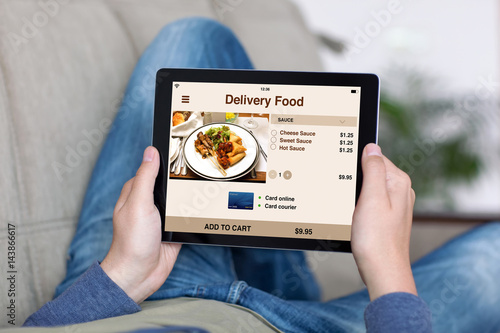 man on sofa holding tablet with app delivery food screen