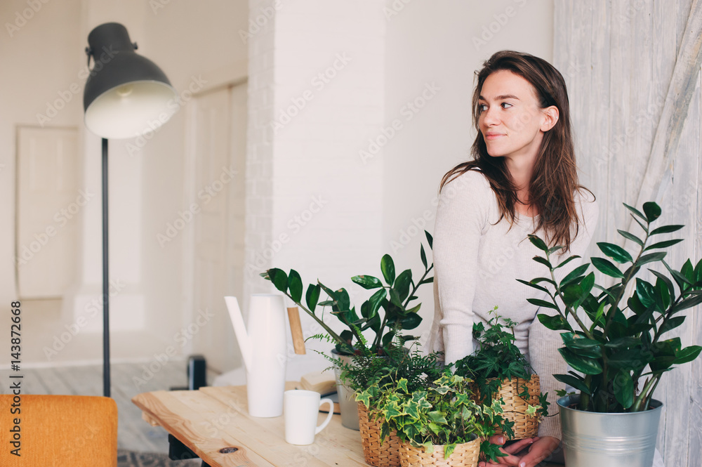 young woman watering flowerpots at home. Casual lifestyle series in modern scandinavian interior young woman watering flowerpots at home. Casual lifestyle series in modern scandinavian interior