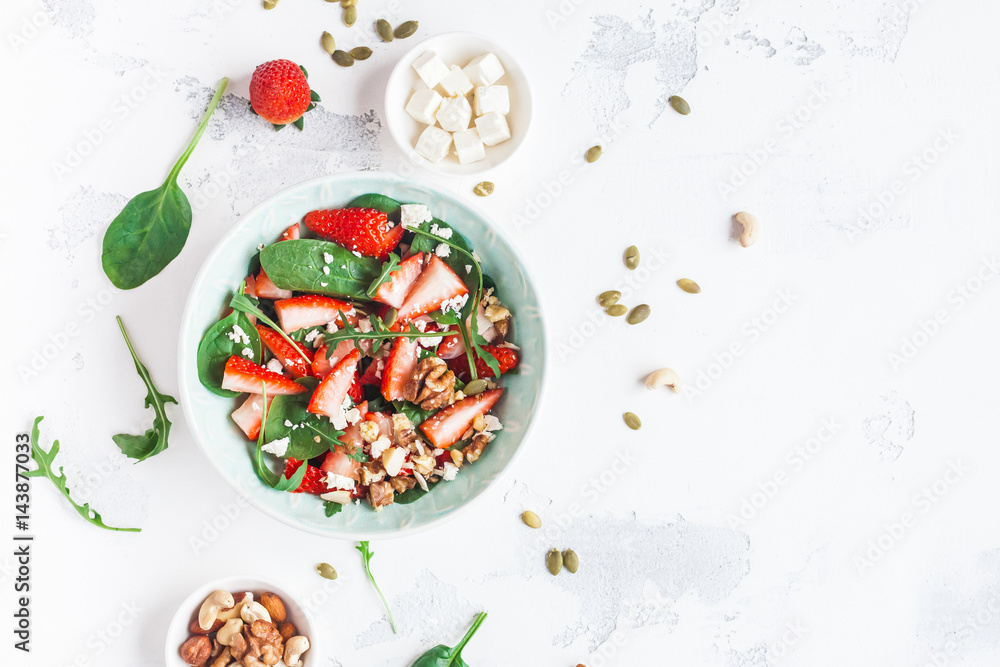 Strawberry salad. Spinach leaves, sliced strawberries, nuts, feta cheese on white background. Healthy food concept. Fat lay, top view Strawberry salad. Spinach leaves, sliced strawberries, nuts, feta cheese on white background. Healthy food concept. Fat lay, top view